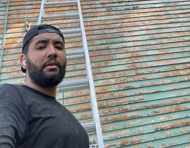 Mateus on a ladder repairing old siding
