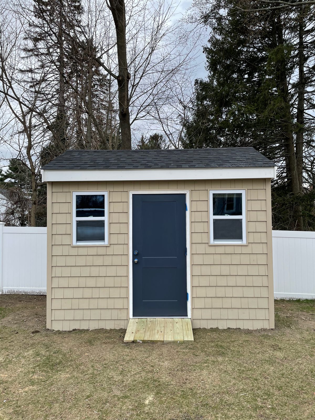Small finished backyard building with gray shingle siding and a navy door