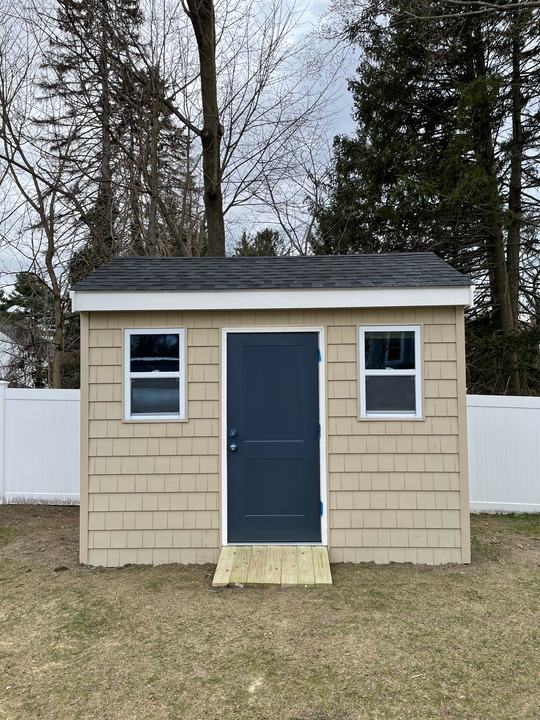 Small finished backyard building with gray shingle siding and a navy door
